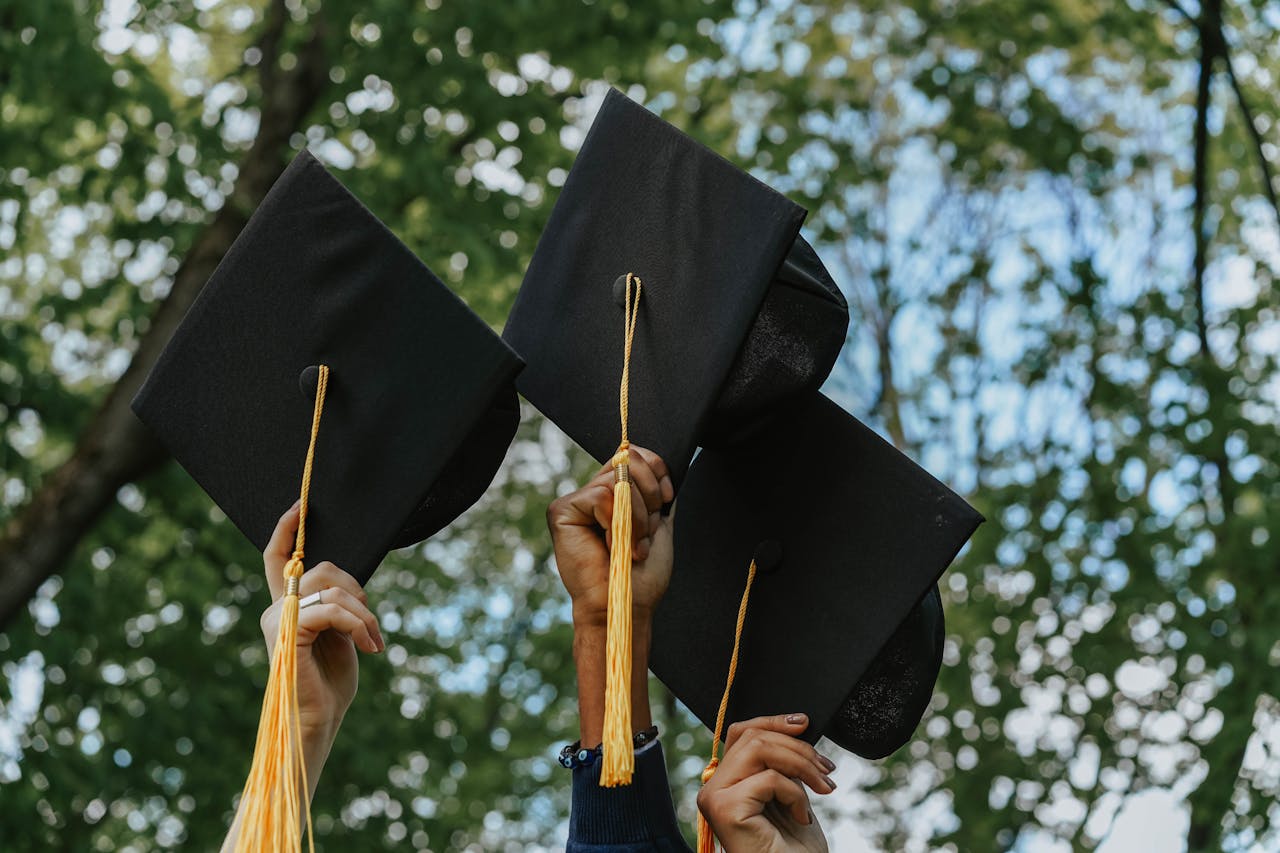 who-we-are Three hands holding graduation caps in celebration, symbolizing success.